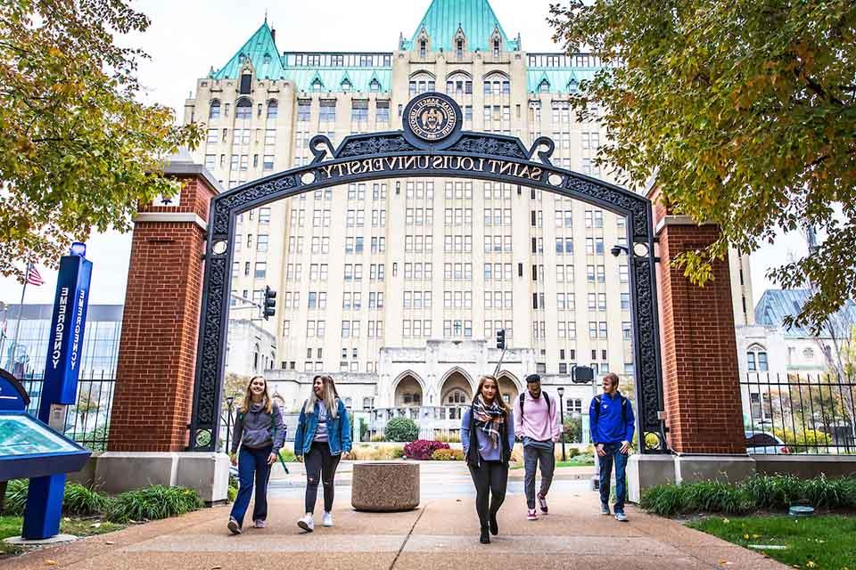 Students walk under an archway that says Saint Louis University on campus.